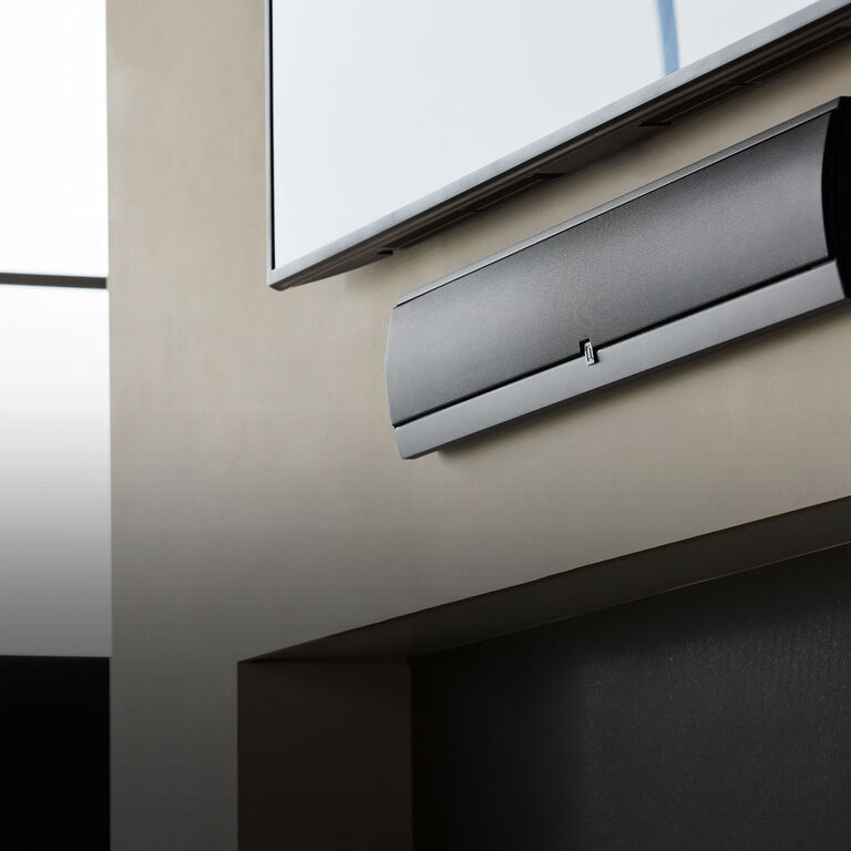 A speaker mounted on an outside wall below a TV.